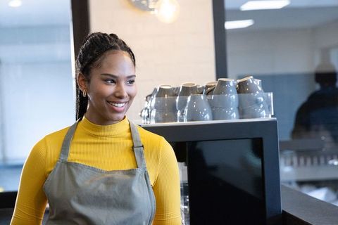 Smiling african american barista working behind espresso machine in sunlit modern cafe
