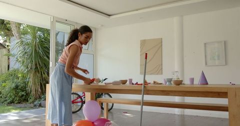 Young woman tidying post-party in bright modern dining room