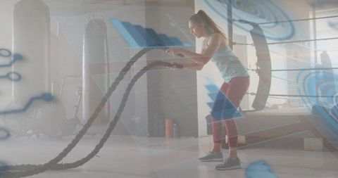Woman powering battle ropes in gym with digital hud overlay, intense fitness training
