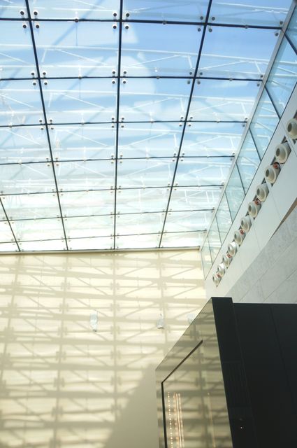 Modern architectural design featuring a glass skylight allowing natural light to filter through, casting patterns on the walls. Perfect for illustrating contemporary building design, creating a bright and airy atmosphere. Ideal for use in articles about architecture, interior design, structural engineering, or urban development.