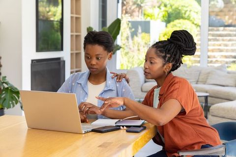 Mentoring teen during online studying at home with laptop and notes
