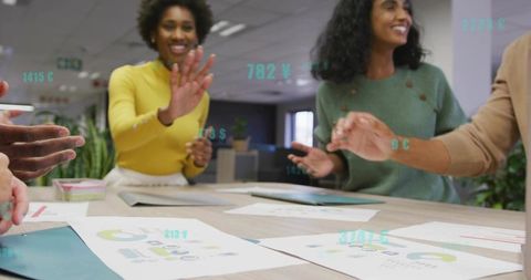 Diverse team high-fiving over charts while collaborating on modern office project