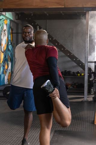 African men stretching and partner spotting in industrial gym loft with graffiti mural