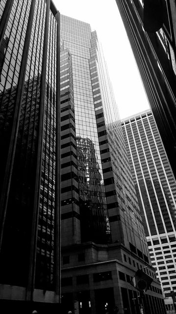 Black and white photo of skyscrapers forming an urban cityscape. High-rise buildings dominate the downtown area, showcasing reflective surfaces and modern architecture. Ideal for use in articles related to urbanization, corporate workplaces, modern architecture studies or city infrastructure analysis.