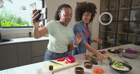 Recording and preparing colorful salad at kitchen island with ring light, diverse women