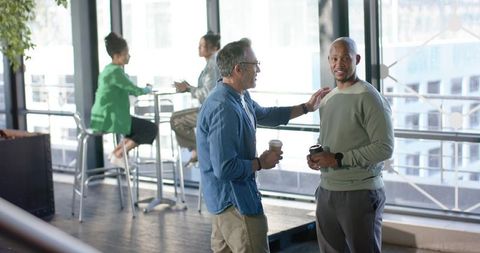 Colleagues chatting over coffee in modern office lounge with panoramic city view