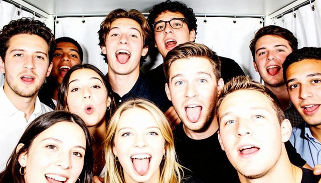 Eleven friends crowding booth celebrating night out with playful, energetic expressions