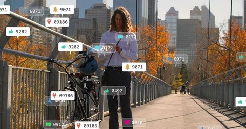 Urban cyclist checking smartphone with floating social notifications on autumn bridge