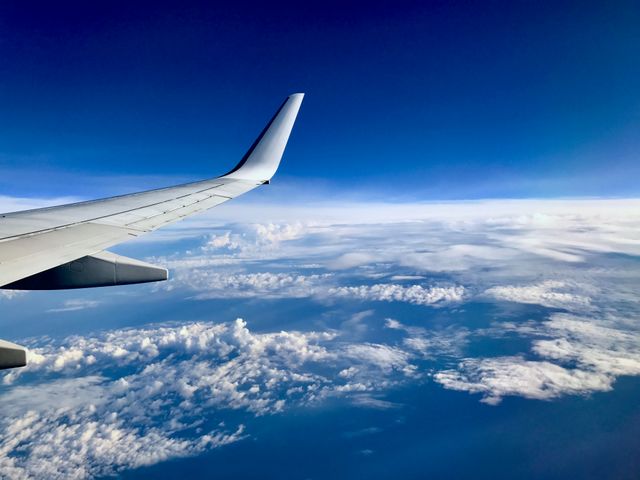 Showing airplane wing over fluffy clouds with clear blue sky in background. Perfect for travel and adventure blogs, airline promotions, flight-related articles, or advertisements aimed at frequent travelers.