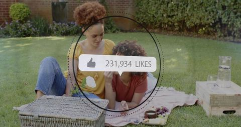 Two women sharing casual picnic on lawn while social media likes counter shows 231,934