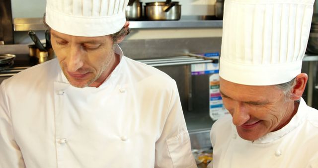 Professional chefs wearing white uniforms and chef hats are working together in a modern commercial kitchen. Suitable for use in articles or advertisements related to culinary arts, professional cooking, restaurants, and chef teamwork.