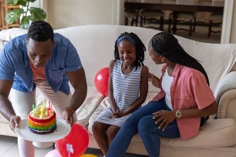 African american family celebrating birthday at home with rainbow cake and balloons