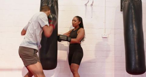 Diverse boxing partners training with heavy bag in urban gym for strength and teamwork