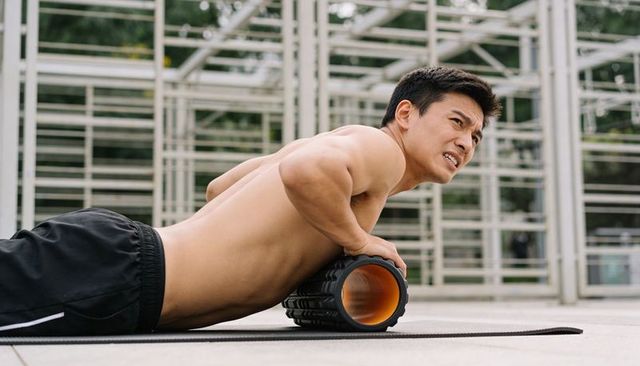 Shirtless man using foam roller for core release and mobility training in outdoor gym