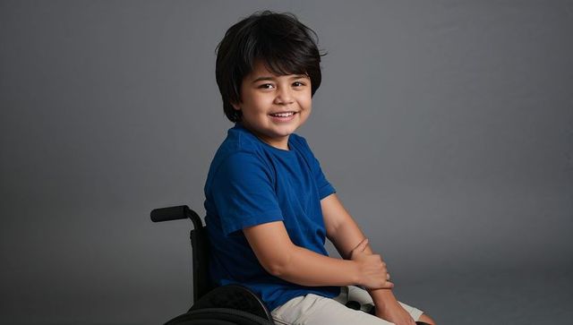 Smiling boy sitting in wheelchair wearing blue t-shirt, conveying joy and inclusion