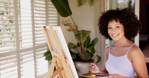 Smiling Artist Painting on Canvas in Sunlit Room