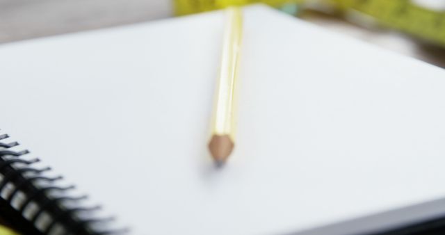 A yellow pencil rests on a blank spiral notebook, with copy space. Ideal for concepts involving education, writing, or creative ideas.