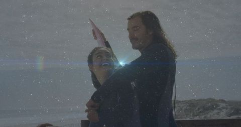 Joyful couple embracing with pink surfboard at foggy beach