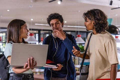 Diverse students collaborating with laptop and notebooks in busy campus study lounge