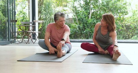 Mature Women Stretching on Yoga Mats in Bright Room with Fitness Trackers