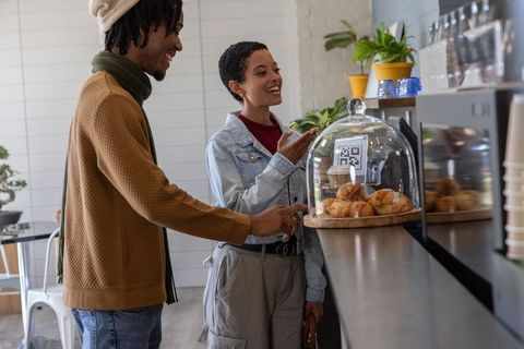 Couple selecting pastries at café counter with qr code under glass dome