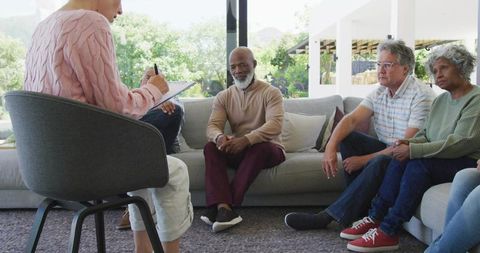 Clinician taking notes during diverse group therapy session in sunlit living room