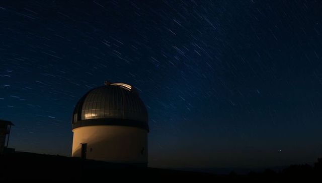 Observatory dome glowing on ridge while star trails sweeping across clear night sky