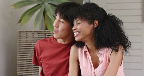 Diverse couple relaxing on sunroom bench surrounded by greenery, cozy intimate moment