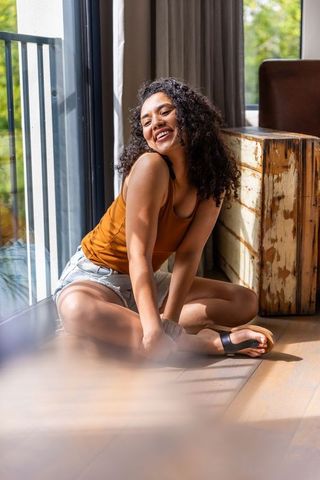 African american woman smiling and relaxing by sunlit balcony door in cozy living room