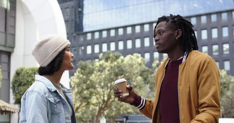 Young diverse friends having coffee and conversation while holding takeout cups in urban plaza