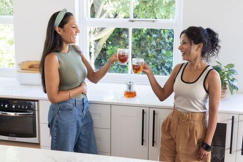 Friends toasting with tea in modern kitchen, indian and african american women