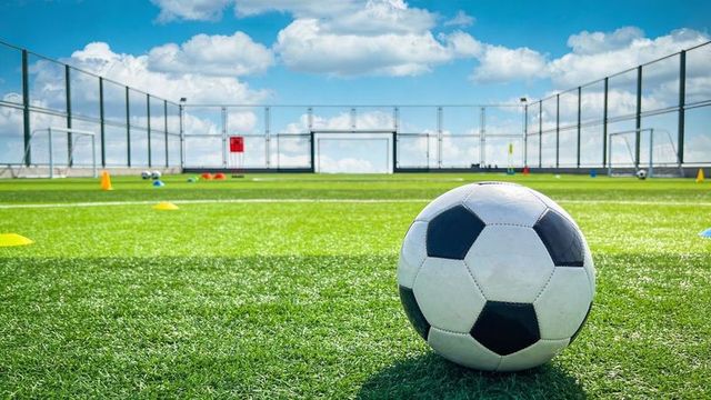 Soccer ball sitting on synthetic turf at training pitch with goals, cones and blue sky