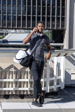African american man talking on phone while carrying gym duffel bag on city rooftop