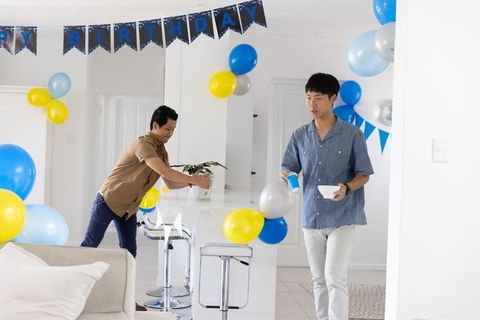 Two asian men decorating modern open-plan kitchen for birthday celebration with blue balloons