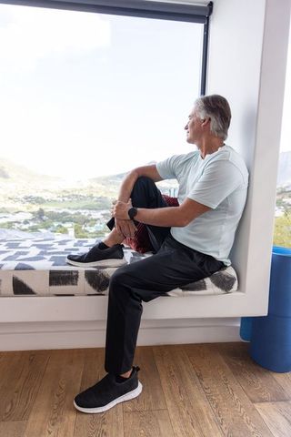 Senior man sitting on window bench gazing at sunlit valley with foam roller, contemplative lifestyle