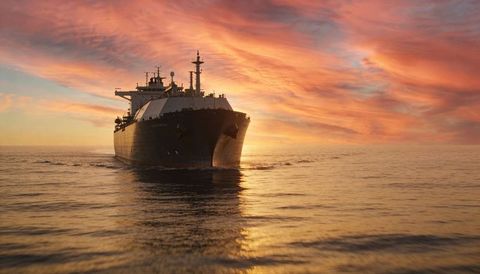 Large tanker gliding across calm ocean at sunset with golden sky and reflective wake