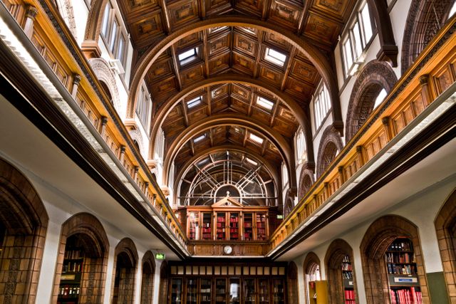 This image showcases the stunning interior of a historic library, featuring a grand arched wooden ceiling and classic bookshelves. Ideal for use in articles or promotions related to education, architecture, history, cultural heritage, and literature. It can also be used in educational brochures, library promotions, and architectural design presentations.