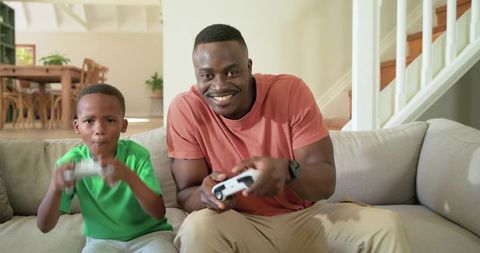 African american father and son playing video games on couch enjoying bonding time
