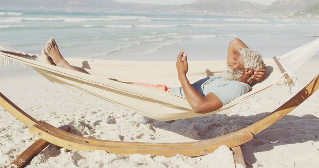 Elderly man laying in hammock on sandy beach reading something. Perfect for illustrating themes of relaxation, vacation, retirement, tranquility, and lifestyle.