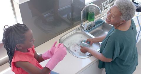 African grandmother and granddaughter washing dishes together in sunlit kitchen