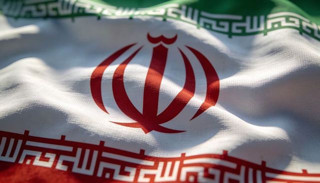 Sunlit waving iran flag close-up showing red emblem and green-red borders on woven cloth