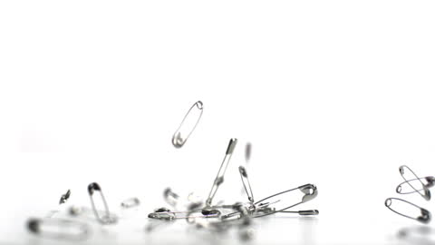 Safety Pins Falling on White Background in Slow Motion