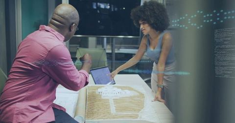 Collaborators discussing architectural scale model and tablet during late-night planning meeting