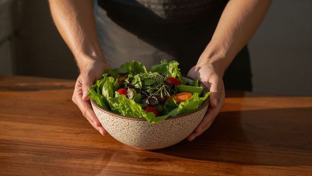 Hands cradling speckled ceramic bowl of fresh garden salad on wooden table
