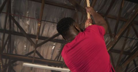 Determined Man Climbing Rope in Industrial Gym