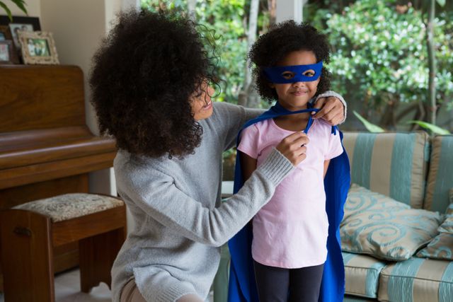 Mother and daughter enjoying playtime at home, with the daughter dressed as a superhero. Ideal for use in parenting blogs, family lifestyle articles, or advertisements promoting family activities and creativity.