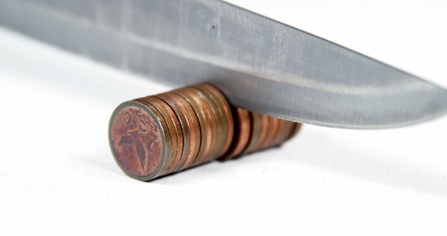 The image shows a knife slicing through a stack of coins, specifically pennies, against a white background. This visual metaphor can be used in topics related to financial planning, budgeting, investment, economic crisis, or cost-cutting. It is suitable for use in blog posts, financial presentations, or economic-themed articles.