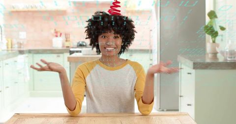 Smiling woman presenting floating digital code overlay with open palms in bright kitchen