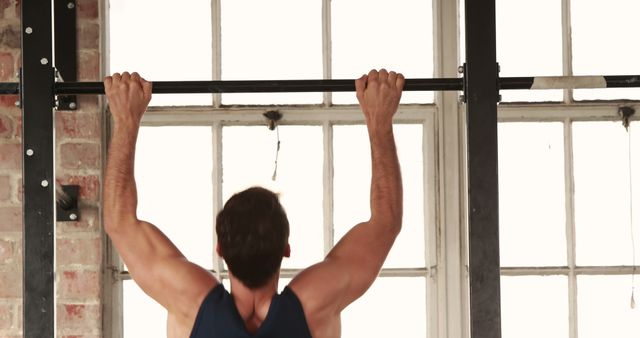 A Caucasian man is engaged in a pull-up exercise at a gym, demonstrating strength and fitness. His workout routine emphasizes upper body conditioning and muscle toning.