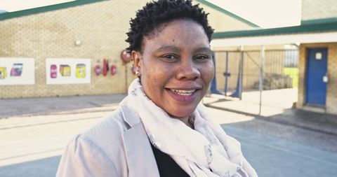 an engaging portrait of a middle-aged african female teacher with short spiky hair, smiling to the camera outdoors in a school playground. this image is well-suited for use in educational content, diversity promotion, teaching materials, school-related advertisements, or community engagement stories.